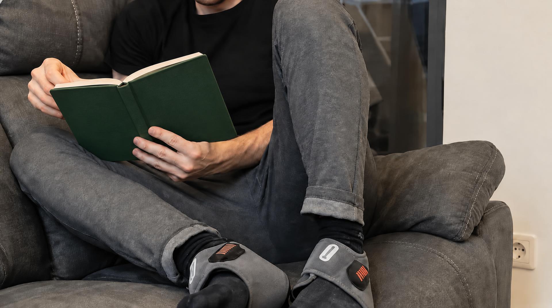 Person reading on the couch while wearing the foot massager wraps